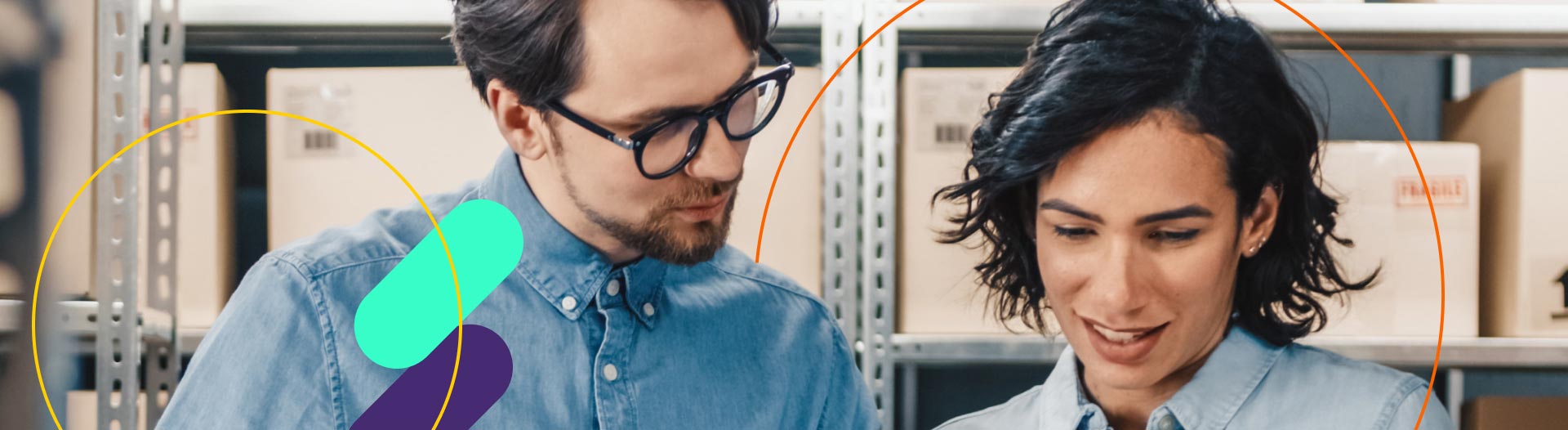 Um homem e uma mulher, ambos de blusões azuis e de cabelos escuros, verificando resultados no tablet, fundo com um estoque cheio de produtos em caixas de papelão.